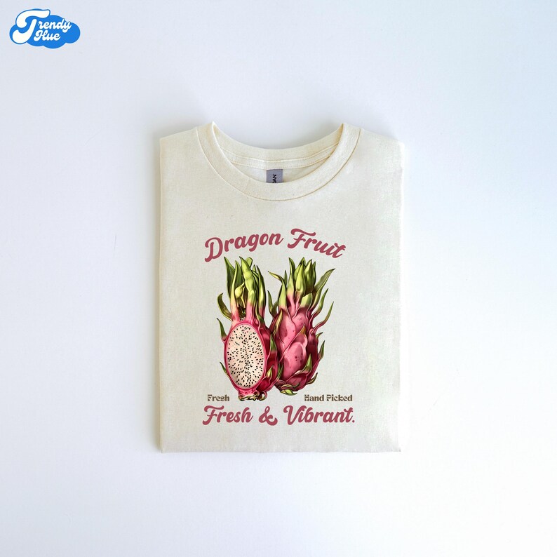 May include: A white t-shirt with a pink and green dragon fruit graphic. The text on the shirt reads 'Dragon Fruit', 'Fresh', 'Hand Picked', and 'Fresh & Vibrant.'