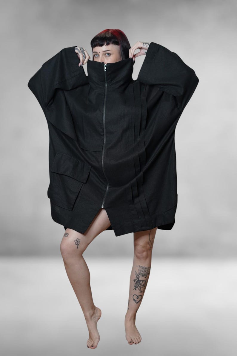 May include: Black oversized jacket with a high collar and a full-length zip. The jacket features large pockets and wide sleeves. The model is wearing the jacket. The jacket is made of a dark fabric.