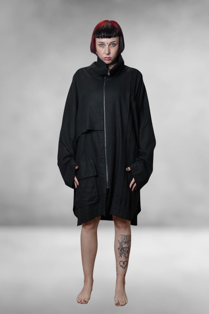 May include: A black, oversized coat with a high collar and a full-length zip. The coat has two large front pockets and long sleeves. The model is standing in front of a grey background.