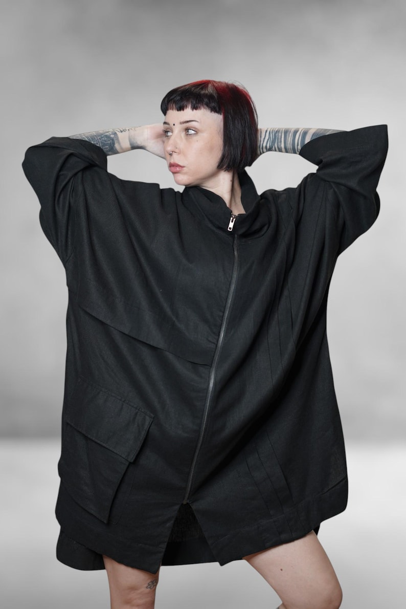 May include: Black oversized jacket with a zip-up front, two large front pockets, and a high collar. The jacket has a relaxed fit and long sleeves. The model is wearing the jacket with their arms behind their head.