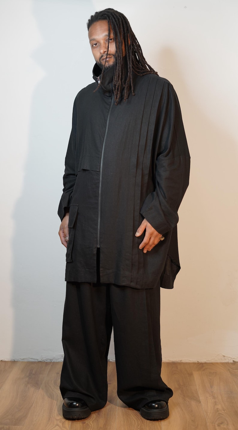 May include: A black outfit comprising a zip-up jacket with a high collar, wide-leg trousers, and black shoes. The jacket features a minimalist design with a vertical seam detail. The outfit is made from a lightweight fabric.