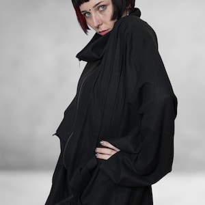 May include: A black, oversized jacket with a high collar and a zip fastening. The jacket features long sleeves and a relaxed fit. The person in the image has short black hair with red highlights.