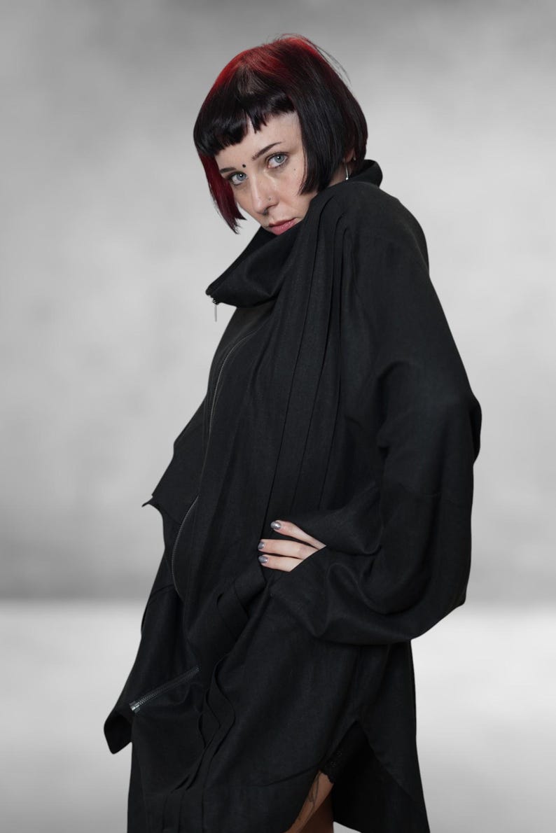 May include: A black, oversized jacket with a high collar and a zip fastening. The jacket features long sleeves and a relaxed fit. The person in the image has short black hair with red highlights.