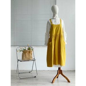 Peut inclure: Une robe en lin jaune avec une blouse blanche en dessous. La robe a une jupe pliss&eacute;e et un design simple. La robe est expos&eacute;e sur un mannequin sur un fond blanc.