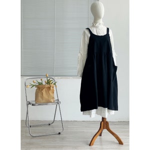 Peut inclure: Une robe en lin noire &agrave; bretelles r&eacute;glables et une jupe pliss&eacute;e. La robe est accroch&eacute;e &agrave; un mannequin blanc avec un chemisier blanc en dessous.