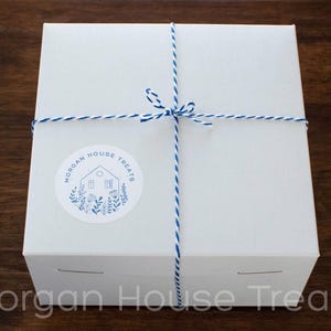 Square white bakery box tied with decorative royal blue and white bakers twine. Blue and white Morgan House Treat logo sticker in lower left corner of the box.