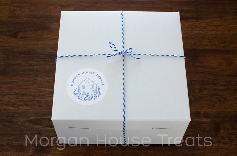Square white bakery box tied with decorative royal blue and white bakers twine. Blue and white Morgan House Treat logo sticker in lower left corner of the box.