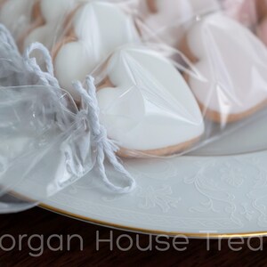 Close up side shot of white baker's twine tie closure with sleeve of cookies fading to right. Cookies rest on white china plate with gold rim. Morgan House Treats watermark at bottom of image.