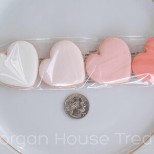 Single sleeve of four pink ombre cookies resting on white china plate with quarter for size reference. Ingredient label on back of sleeve slightly visible on white plate background. Morgan House Treats watermark at bottom of image.