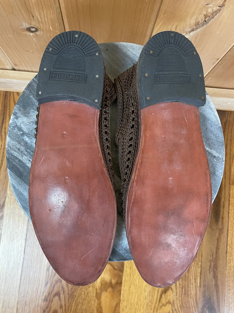 K&ouml;nnte beinhalten: Ein Paar braune, geh&auml;kelte Lederschuhe mit brauner Ledersohle. Die Sohlen tragen den Schriftzug "Seashells".