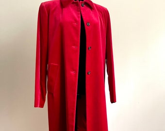 May include: A red velvet coat with a classic collar and button-down closure. The long coat features long sleeves and a tailored fit, displayed on a black mannequin. The coat has a single pocket on the left side.
