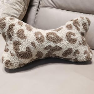 Op de afbeelding: Een botvormig kussen met een crèmekleurige achtergrond en een bruine luipaardprint. Het kussen is gemaakt van een zacht, getextureerd materiaal. Dit decoratieve kussen is ontworpen voor comfort en voegt een vleugje stijl toe aan elke woonruimte.