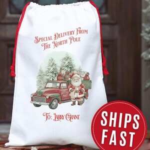 May include: White drawstring gift bag with red accents. The bag features a vintage illustration of Santa Claus with a red truck delivering gifts. Text on the bag reads "Special Delivery From The North Pole" and "To: Larry Grant". A red circle with "SHIPS FAST" is also visible.