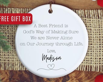 May include: A white ceramic ornament with a gold string for hanging. The ornament has the text "A Best Friend is God's Way of Making Sure We are Never Alone on Our Journey through Life. Love, Madison" and a heart design. A red box with the text "FREE GIFT BOX" is in the upper left corner.