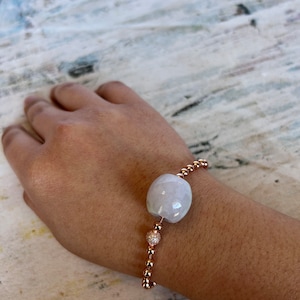 May include: A rose gold bracelet with a large white gemstone bead and smaller rose gold beads with clear stones.