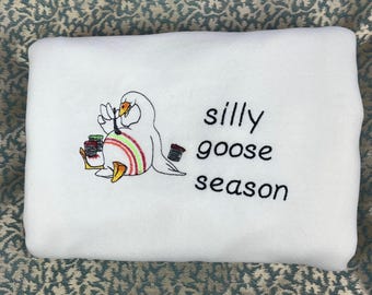 May include: White sweatshirt with an embroidered image of a goose holding a spool of thread and the text "silly goose season".