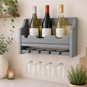 May include: A gray wooden wine rack holding three wine bottles labeled Pinot Grigio, Merlot, and Sauvignon Blanc. Four wine glasses hang below. The rack is mounted on a wall above a countertop.