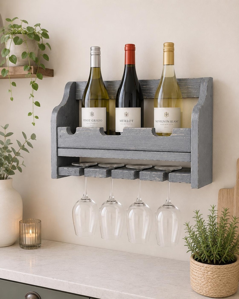 May include: A gray wooden wine rack holding three wine bottles labeled Pinot Grigio, Merlot, and Sauvignon Blanc. Four wine glasses hang below. The rack is mounted on a wall above a countertop.