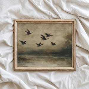 May include: A framed vintage-style painting featuring a flock of birds in flight over a body of water. The artwork has a muted color palette of browns, greens, and grays, with a wooden frame. The painting evokes a sense of tranquility and nature.