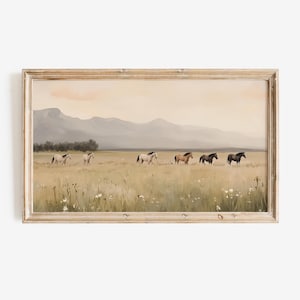 May include: A framed landscape print featuring a field of tall grass and wildflowers with a herd of horses. The horses are various shades of brown and black. Mountains and a soft peach sky are in the background.