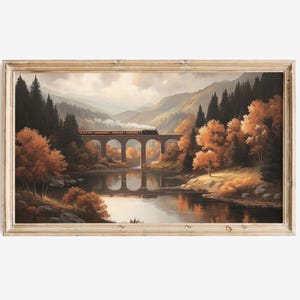 Könnte beinhalten: Gerahmtes Landschaftsgemälde, das einen Zug zeigt, der eine Steinbrücke über einen ruhigen Fluss überquert. Die Szene zeigt Herbstlaub in Orange- und Brauntönen, mit Bergen im Hintergrund. Das Kunstwerk ist in einem Holzrahmen gefasst.