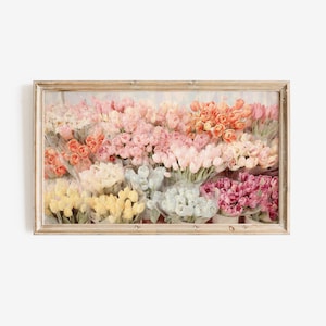 以下が含まれることがあります： さまざまな色のチューリップが鮮やかに並んだ、額入りの花のプリント。 チューリップは列に並んでおり、ピンク、オレンジ、黄色、白の色合いを示しています。 アートワークは明るい色の木製フレームに収められています。