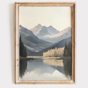 May include: A framed painting of a mountain lake scene. The lake is calm and reflects the mountains and trees surrounding it. The mountains are a light blue and gray color, and the trees are a dark green. The sky is a light blue.