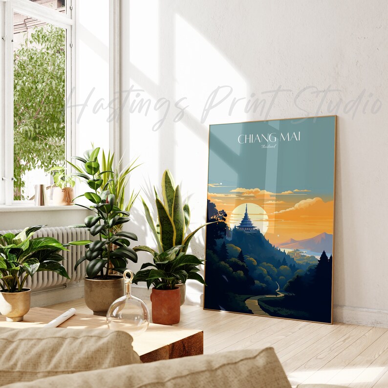 May include: A vintage-style travel poster with a gold frame featuring a scenic view of Chiang Mai, Thailand. The poster depicts a mountain range with a temple at the peak, a winding road, and a sunset sky with a large sun.