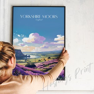 Może przedstawiać: Ramka z plakatem przedstawiającym kolorową ilustrację krajobrazu z fioletowymi kwiatami i rzeką. Plakat zawiera tekst "YORKSHIRE MOORS England" u g&oacute;ry.