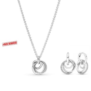 May include: A silver jewellery set comprising a necklace and matching earrings. The necklace features a chain with a pendant of intertwined circles. The earrings are hoop style with three connected circles. The jewellery is embellished with small, clear stones.