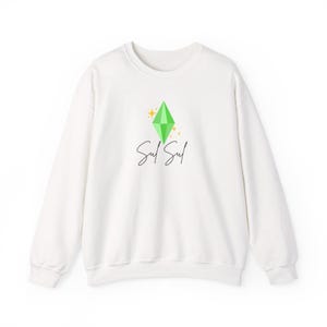 May include: White crewneck sweatshirt featuring a green diamond graphic with gold sparkles and the text "Sul Sul" in a handwritten font. A casual, comfortable top for everyday wear.