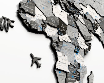 Puede incluir: Un mapa del mundo en 3D con textura de madera. El mapa está en tonos grises y negros con líneas azules que representan ríos y carreteras. El mapa está inclinado para mostrar África en primer plano. Un pequeño icono de avión se encuentra en la esquina inferior izquierda de la imagen.