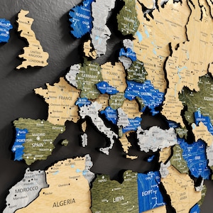 Op de afbeelding: Een gedetailleerde houten wereldkaart met landen in verschillende kleuren, waaronder blauw, groen en beige. Grote steden en namen van landen zijn in het wit aangegeven. De kaart is gemonteerd op een donkergrijze achtergrond.