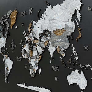 May include: A 3D wooden world map with a black background. The map is made of different shades of grey and brown wood. The continents are raised and the oceans are recessed. The map includes the names of the continents and oceans.