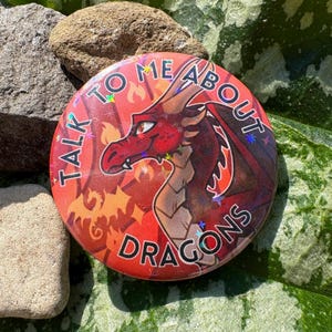 Könnte beinhalten: Ein runder Button mit dem Text "TALK TO ME ABOUT DRAGONS", der eine rote Drachenillustration umgibt. Der Drache hat rote Schuppen und einen ernsten Gesichtsausdruck. Der Hintergrund ist ein Farbverlauf von Rot und Orange.