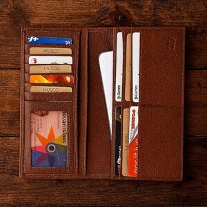 May include: Open brown leather wallet with multiple card slots filled with cards. The wallet is on a wooden surface. Cards include "MUSCO" and "revantsiaas" with a colorful design.