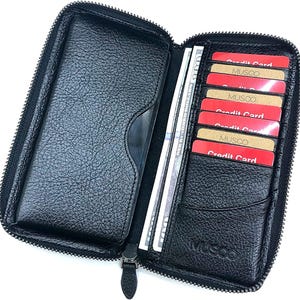 May include: Open black leather wallet with a zipper closure. The wallet is open, revealing multiple credit cards, cash, and a clear ID holder. The credit cards are red and gold, with the brand name "MUSCO" visible.
