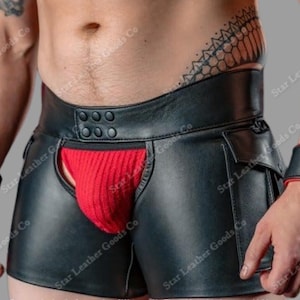 Puede incluir: Shorts de cuero negro con una bolsa roja y puños a juego. Los shorts tienen una cintura ancha con botones y pequeños bolsillos. Los puños tienen ribetes rojos. La imagen tiene el texto "Star Leather Goods Co".
