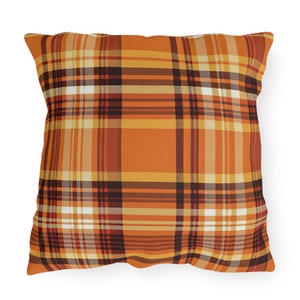 May include: Square throw pillow with a plaid pattern in shades of orange, brown, and cream. The pillow features a classic tartan design, with intersecting lines creating a grid-like appearance. The pillow is a decorative item for a home.