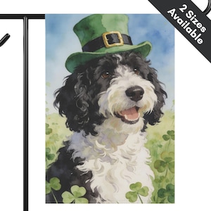 May include: A watercolor illustration of a black and white dog wearing a green leprechaun hat, set against a backdrop of green shamrocks and a blue sky. The dog is smiling with its tongue out. The text "2 Sizes Available" is in the upper right corner.