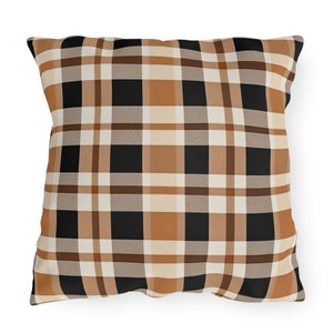 May include: Square throw pillow with a plaid pattern in black, tan, cream, and brown. The pillow has a classic buffalo check design, perfect for adding a touch of rustic charm to any living space. The pillow is a square shape.