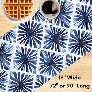 May include: A white table runner with a blue floral pattern. The runner is 16 inches wide and available in 72 or 90 inches long. A plate with a waffle and a cup of coffee are on the table runner.