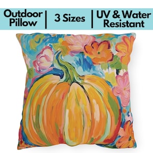 May include: Outdoor pillow with a vibrant pumpkin and floral design. The pillow features a large orange pumpkin with a green stem, surrounded by colorful flowers in shades of pink, orange, and blue. The text on the pillow says "Outdoor Pillow", "3 Sizes", and "UV & Water Resistant".