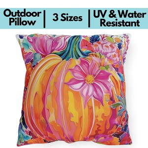 May include: Square outdoor pillow with a vibrant floral pumpkin design. The pillow features a large orange pumpkin with pink and yellow accents, surrounded by colorful flowers and foliage. Text on the pillow reads "Outdoor Pillow", "3 Sizes", and "UV & Water Resistant".