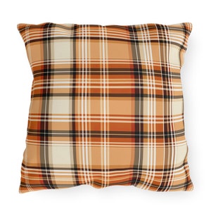May include: Square throw pillow with a plaid pattern in shades of orange, cream, black, and white. The pillow features a classic tartan design, perfect for adding a touch of warmth and style to any living space. The pillow is a decorative home accent.