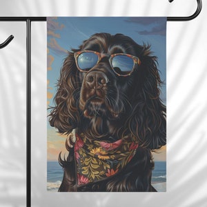 May include: A black dog with brown fur wearing sunglasses and a floral bandana. The dog is looking directly at the camera. The background is a blue sky with clouds and a beach.