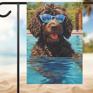 May include: A brown dog with blue sunglasses is swimming in a pool. The dog is looking at the camera with its tongue sticking out. The pool is surrounded by palm trees and a blue sky.