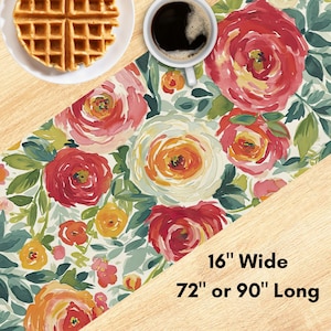 May include: Floral table runner with a watercolor design featuring red, orange, and white roses, and green leaves. The runner is 16 inches wide and available in 72 or 90 inches long.