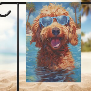May include: A brown and white dog wearing blue sunglasses is in the water. The dog is smiling and has its tongue sticking out. The dog is in front of a blue ocean and a beach with palm trees.
