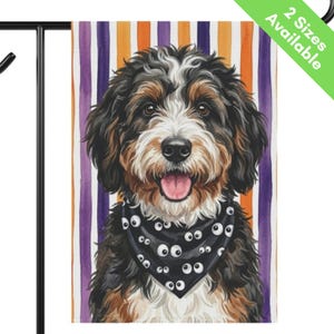 May include: A rectangular garden flag featuring a portrait of a fluffy tricolor dog with black, brown, and white fur. The dog has an open mouth with a pink tongue and wears a black bandana patterned with white googly eyes against a striped background.